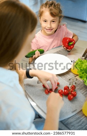 Foto Bild Kind Mädchen hilft Mama, frisches Gemüse zu kochen und zu schneiden.