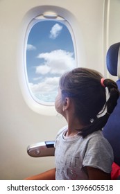 Sweet little girl on a plane seat, watching mesmerized the clouds in the sky through the window during the flight on a beautiful sunny day