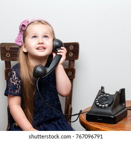 A Sweet Little Girl Is Ringing On The Old Phone. The Concept Of A Happy Childhood, Retro Style, Old Things Of The Fifties Of Last Century.