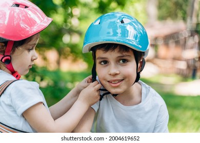 Sweet little sister helps her brother to fasten his protective helmet. Kids have fun outdoors - Powered by Shutterstock