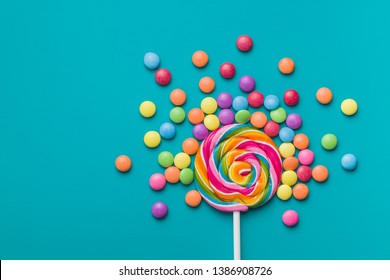 Sweet lollipop and colorful chocolate candy pills on blue background.