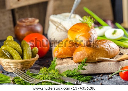 sweet meat pies, bun, bread, dough on a wooden vintage chopping old rustic board, chili, with tomatoes, greens, rice in a pouch, onions, gherkins, cucumbers, on the table top, side and side, bottom sh