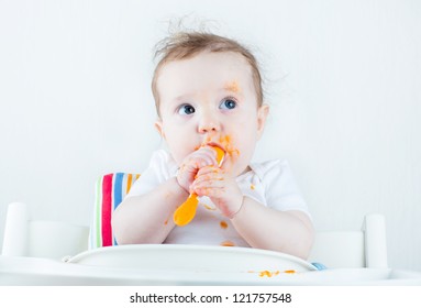 Sweet Messy Baby Eating A Carrot In A White High Chair