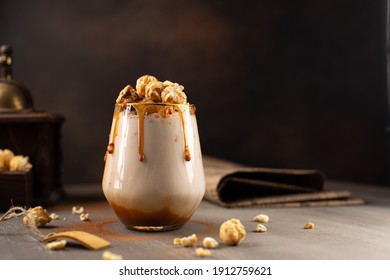 Sweet Milkshake with caramel syrup,cream liqueur,caramel popcorn and chocolate powder on brown background with vintage,manual coffee grinder. - Shutterstock ID 1912759621