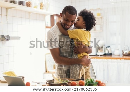 Sweet moments of fatherhood concept. Cute African American boy embracing and kiss on cheek his father while prepare spaghetti meal together in kitchen at home. Happy Black family activity together.