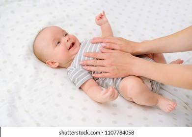 Sweet moments of parenting. Mother's hands gently touch her adorable baby boy, he responds smiling happily. Mother’s care. 