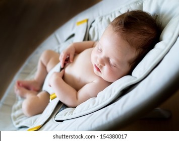 Sweet newborn baby girl sleeping in a bouncer chair in a dark room