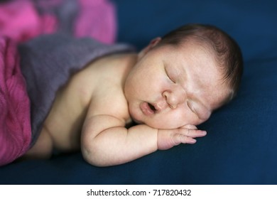 sweet newborn baby sleeps on his stomach on his hands in the real interior, dark blue background close-up