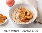 Sweet oatmeal porridge with baked apple slices, cinnamon and caramel sauce in a gray bowl on a light background, top view. Delicious homemade food.