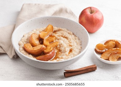 Sweet oatmeal porridge with baked apple slices, cinnamon and caramel sauce in a gray bowl on a light background, top view. Delicious homemade food. - Powered by Shutterstock