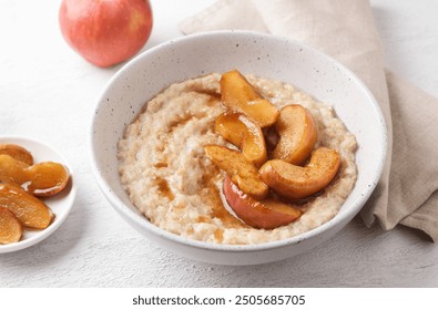 Sweet oatmeal porridge with baked apple slices, cinnamon and caramel sauce in a gray bowl on a light background, top view. Delicious homemade food. - Powered by Shutterstock