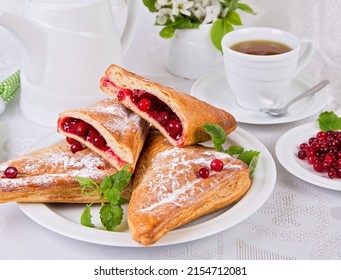sweet pastries with red currant berries, with mint leaves, on a white dish, a cup of tea on a white background - Shutterstock ID 2154712081