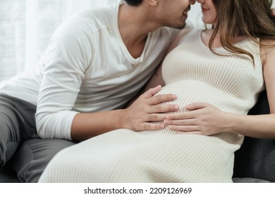 Sweet Pregnant Asian Couple Is Showing Off The Love To Each Other. Their Hands Are Rubbing On The Wife's Tummy With Love Of Parenthood. Selective Focus, Happy Asian Family.