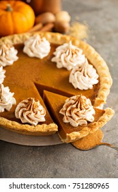 Sweet pumpkin pie decorated with whipped cream and cinnamon with a slice taken out