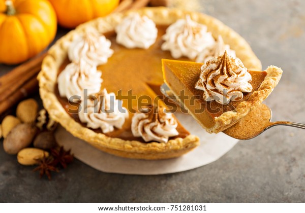 Sweet pumpkin pie decorated with whipped cream
and cinnamon with a slice taken
out