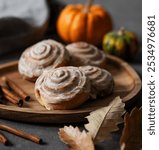 Sweet rolls with cinnamon and icing on a wooden board on a dark background with pumpkin. Concept traditional Swedish buns for breakfast in rustic style. Cozy autumn homemade baking.