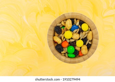 Sweet And Salty Trail Mix In A Bowl On A Yellow Painted Background Overhead View.