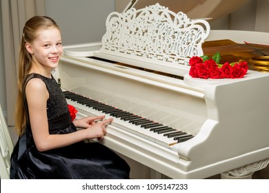 A sweet schoolgirl girl sits beside a white grand piano on which lies a bouquet of flowers. The concept of studying music, spring mood, happy people.