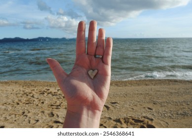 Sweet Sentimental Heart-Shaped Rock Found on a Rocky Beach on the Shores of Okinawa Japan at Nago Beach, Held in a Hand with the Ocean Waves in the Background - Powered by Shutterstock