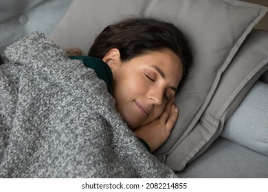 Sweet sleep. Carefree latina female nap on cozy couch alone put folded hands under cheek enjoy nice night dreams. Peaceful young latin lady with closed eyes relax on sofa covered with warm soft plaid