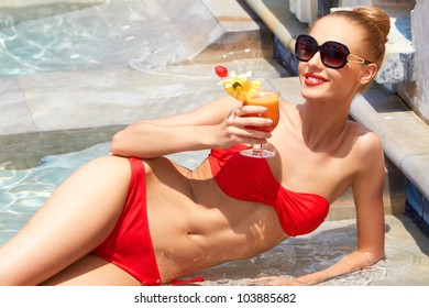 Sweet Smile On A Gorgeous Blonde Woman In A Small Bikini Holding A Tropical Drink In Her Hand While Laying Poolside
