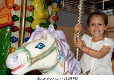 A Sweet Smiling Child Is Sitting On Horse In Carousel