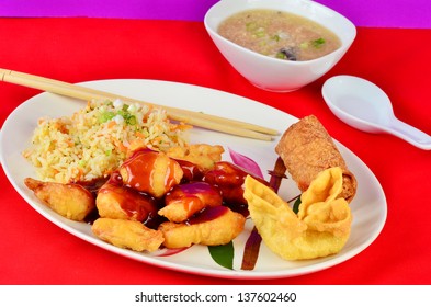 Sweet And Sour Chicken With Fried Rice On Oriental Pattern On Plate.  Served With Hot And Sour Soup, Crab Rangoon And Egg Roll Against Colorful Red And Purple Background.