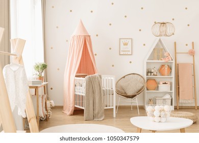 Zoete, ruime kinderkamer interieur voor een baby meisje met witte meubels, pastel roze decoraties en gouden stippen behang