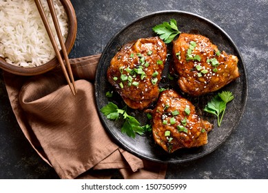 Sweet And Spicy Honey Grilled Chicken Thighs And Bowl Of Rice Over Dark Stone Background. Tasty Food In Asian Style. Top View, Flat Lay