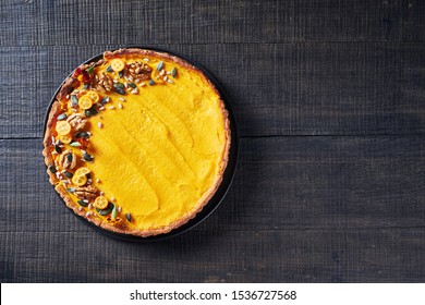 Sweet And Spicy Pumpkin Tart With Orange, Canned Pumpkin Puree, And Cream Filling, Decorated With Kumquat, Walnuts, Pumpkin Seeds, Flowers On A Dark Wooden Background, Copy Space