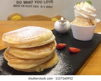 Sweet stack of pancakes with maple syrup and ice cream vanilla on black plate.