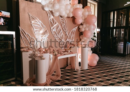 Sweet stand with cakes, macaroons, candies near pink wall decorated with air balloons. Birthday celebration at modern restaurant. Beautiful details of thematic party.