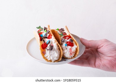 Sweet Tacos With Thin Waffle, Cottage Cheese Cream And Strawberry Topped With Chocolate And Mint On The White Ceramic Plate In Man's Hand