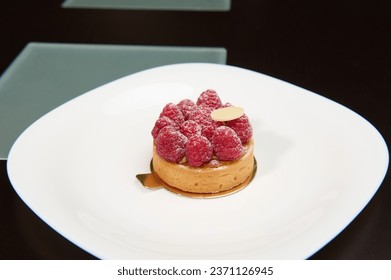 A sweet tartlet with raspberries on a white plate over wooden background. French patisserie and boulangerie
