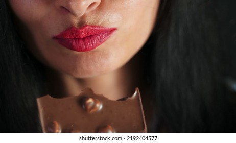 Sweet Temptation. Cropped Closeup Of A Red Lipped Female Biting On A Chocolate, Lips Of Beautiful Sexy Brunette Woman Eating Chocolate With Hazelnuts. High Quality Photo