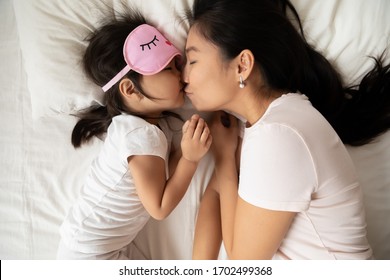 Sweet Tender Moment Of Mom Kiss Child Close Up Top View. Loving Mum Puts Child To Healthy Day Night Sleep, Asian Family Lying In Bed, Kid Girl Wears Pink Sleeping Eyemask. Love Health Care Concept