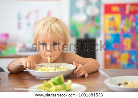 Sweet toddler boy, eating spaghetti at home, making a mess and having fun playing with them
