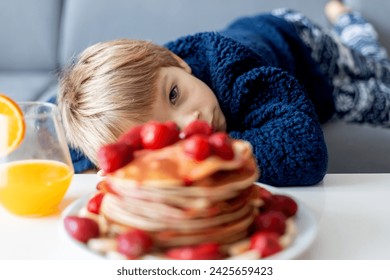 Sweet toddler child, boy, eating american pancakes with strawberries and bananas, topped with syrup and drinking fresh orange juice - Powered by Shutterstock