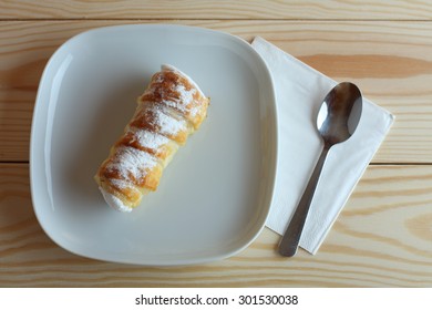 Sweet tube filled egg white, Czech confection called Kremrole on white plate on wooden table.