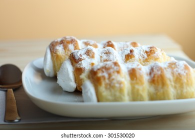 Sweet tubes filled egg white, Czech confection called Kremrole on white plate on wooden table.