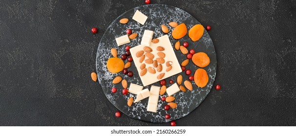 Sweet white chocolate with almond nuts and dried apricots on dark background