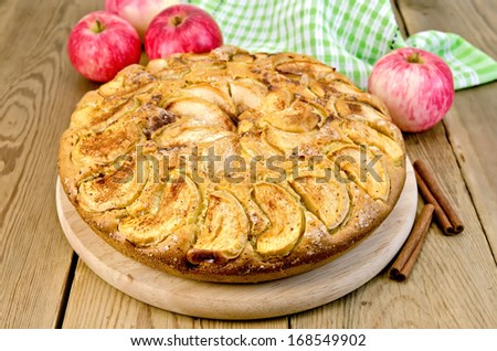 A sweet whole apple pie, napkin, cinnamon on a wooden boards background