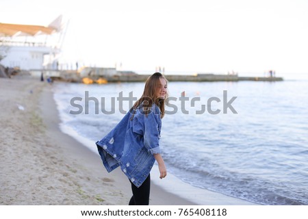 Sweet woman walks and poses in camera, smiles and laughs widely, raises hands up and starts happily whirling on spot, taking off jacket from shoulders. European-looking girl with medium-length blond