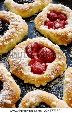 Sweet yeast buns with the addition of berry fruits and butter crumble, sprinkled with powder sugar on a black background, focus on the roll with strawberries, close up view