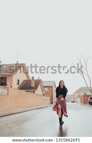 Sweet young girl smiling and getting wet in the rain with black boots and long printed skirt