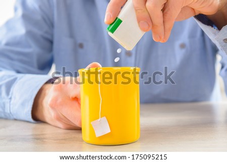 Sweetener tablets and hand with box whit cup of tea