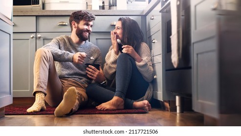 The sweetest moments don't need much. Shot of a happy young couple sharing a tub of ice cream in their kitchen at home.
