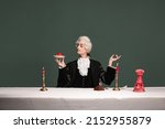 Sweets, cakes. Portrait of young elegant man in peruke and vintage jacket sitting at table isolated on dark green background. Retro style, comparison of eras concept.