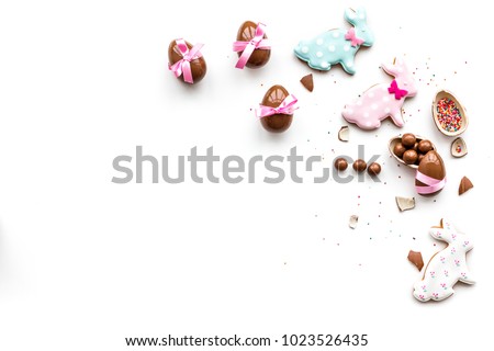Sweets for Easter table. Chocolate eggs near cookies in shape of Easter bunny on white background top view copy space