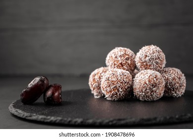 Sweets made of dates and coconut shavings without sugar on a slate Board near the dates